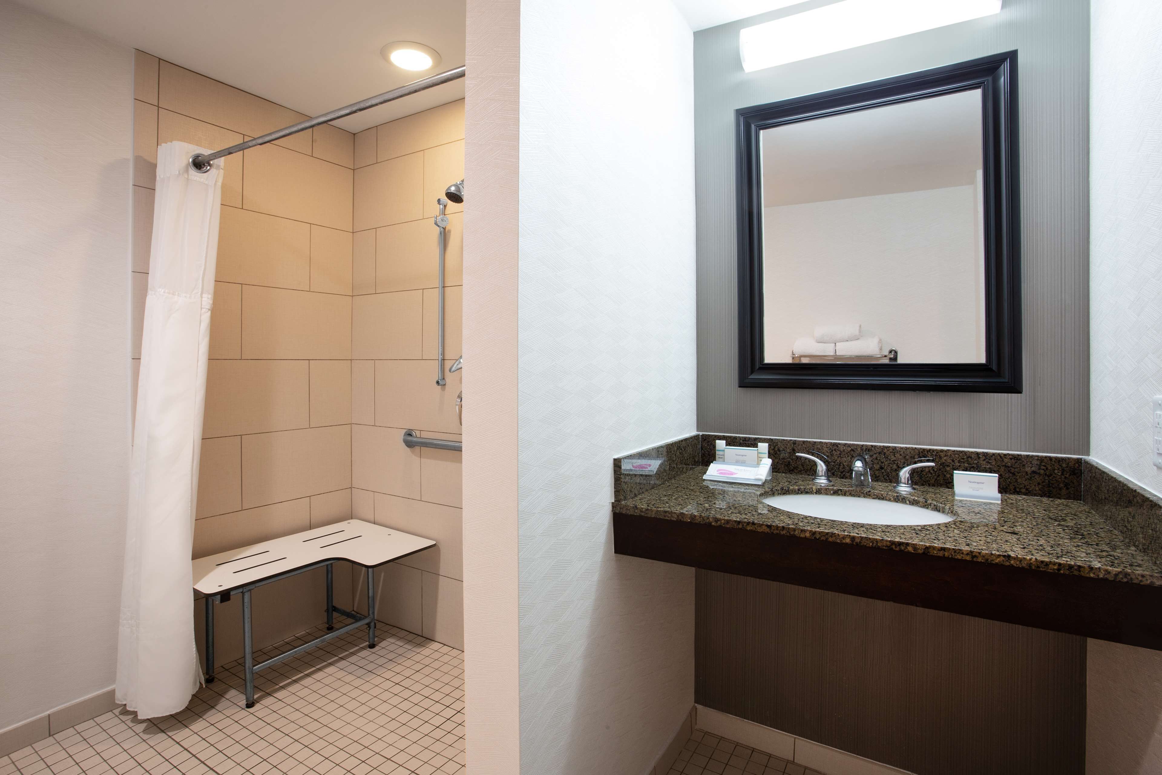 A bathroom with a shower, a bench, a sink, and a mirror.