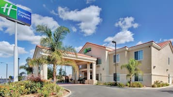 A Holiday Inn Express hotel with a covered entrance, palm trees, and a clear blue sky.