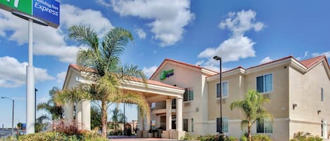 A Holiday Inn Express hotel with a covered entrance, palm trees, and a clear blue sky.