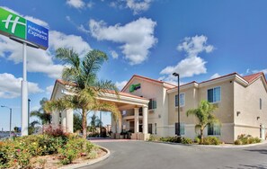 A Holiday Inn Express hotel with a covered entrance, palm trees, and a clear blue sky. - Holiday Inn Express Delano by IHG (Delano)