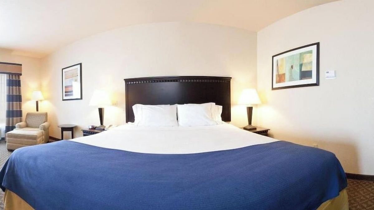 A hotel room with a large bed, two bedside tables, a chair, and two wall-mounted lamps.