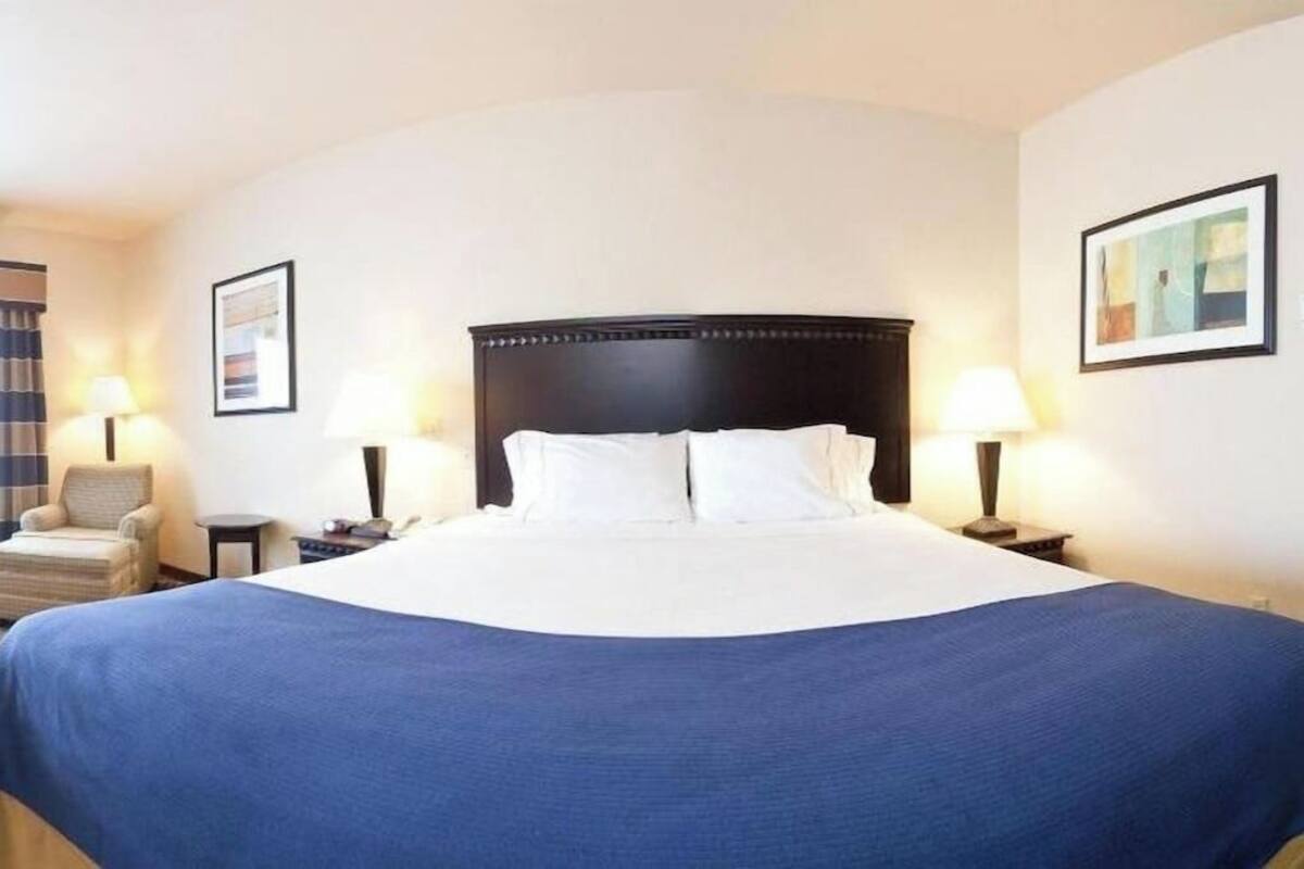 A hotel room with a large bed, two bedside tables, a chair, and two wall-mounted lamps.