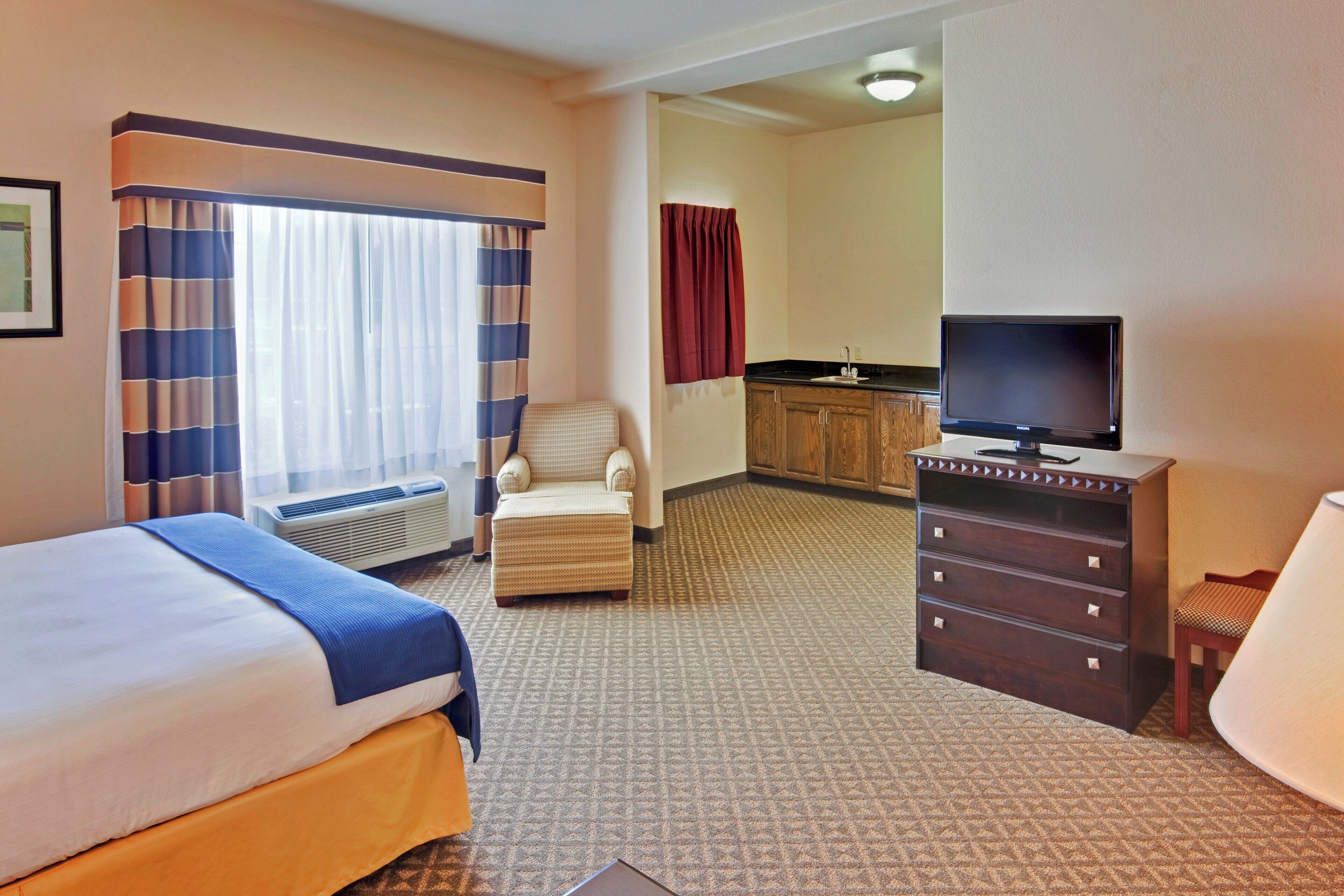 Una habitación de hotel con cama, una silla, televisión y kitchenette.