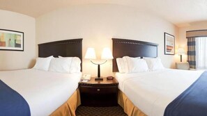 A hotel room with two beds, a nightstand with a lamp, a phone, and a small table with a lamp.