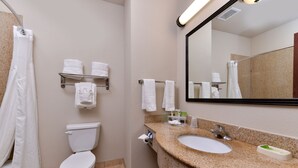 A bathroom with a toilet, sink, and mirror. There are towels on a shelf and a shower curtain.