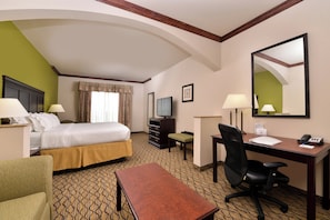 Habitación de hotel con cama, escritorio, silla, televisor y espejo.
