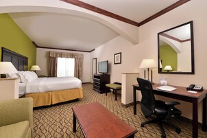 Habitación de hotel con cama, escritorio, silla, televisor y espejo.