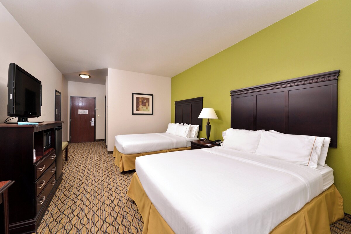 A hotel room with two beds, a television, a desk, and a patterned carpet.