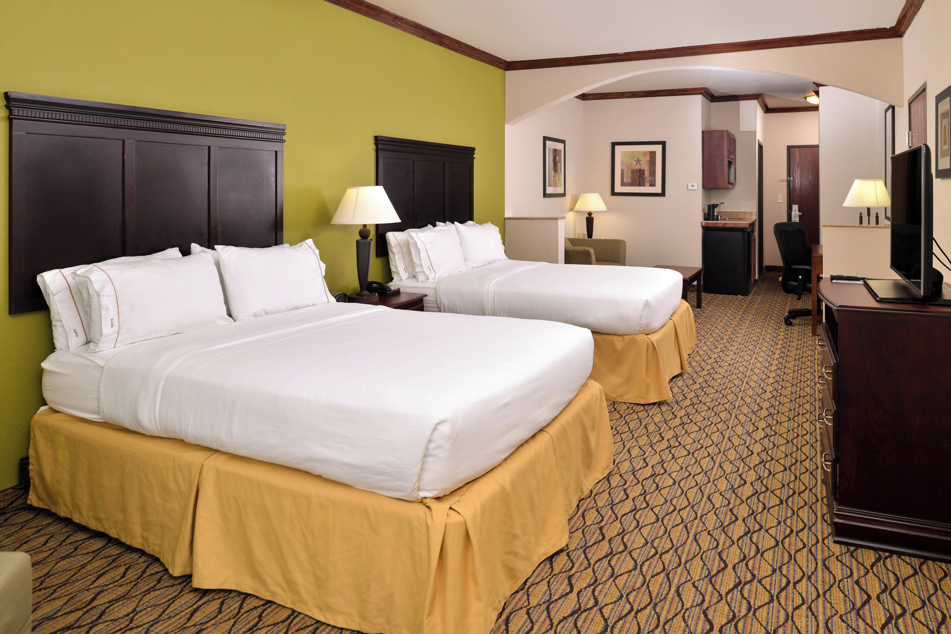 A hotel room with two beds, a desk, a chair, a television, and a bathroom visible through an archway.