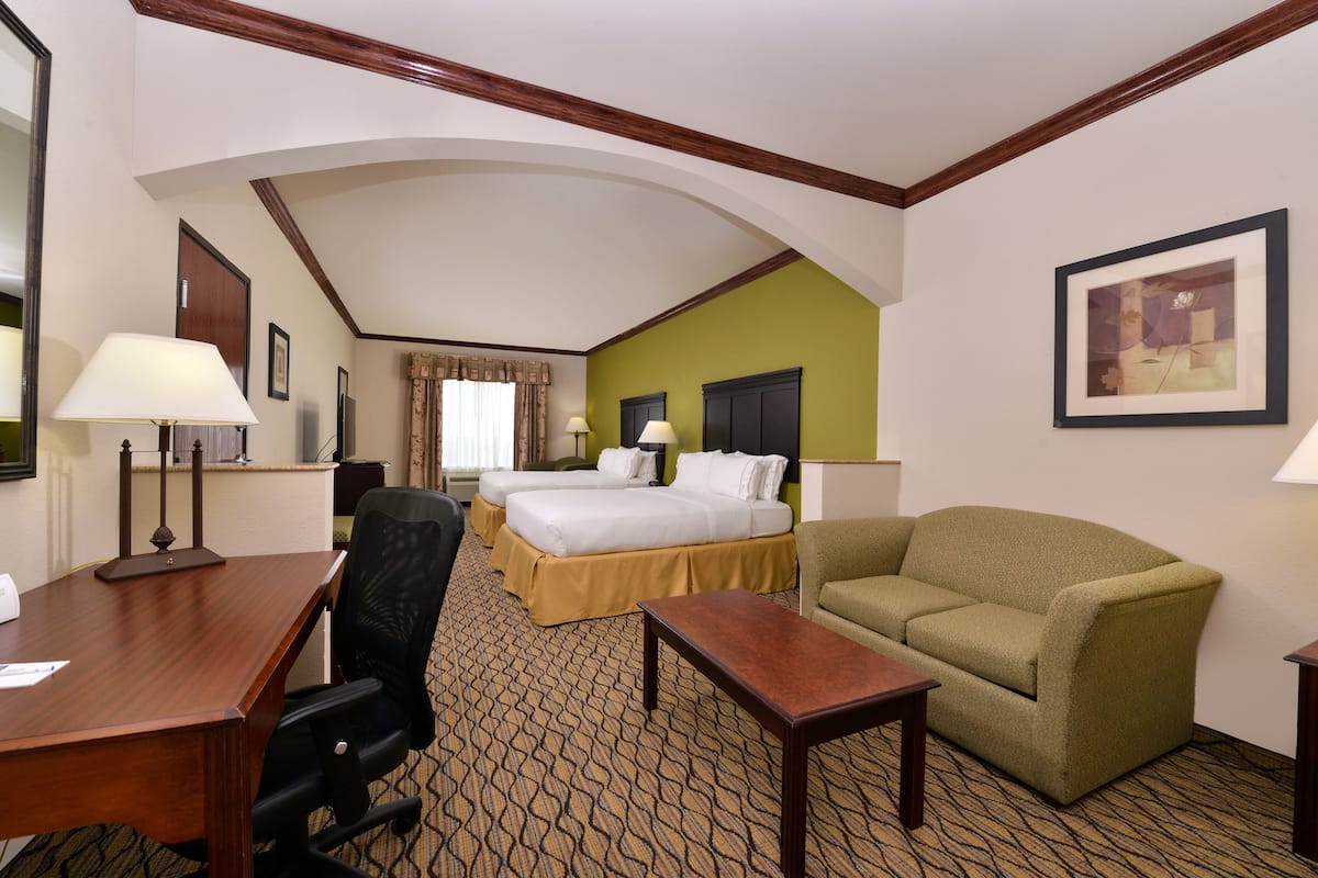 A hotel room with a wooden desk, two beds with yellow bedspreads, a green sofa, and a patterned carpet.
