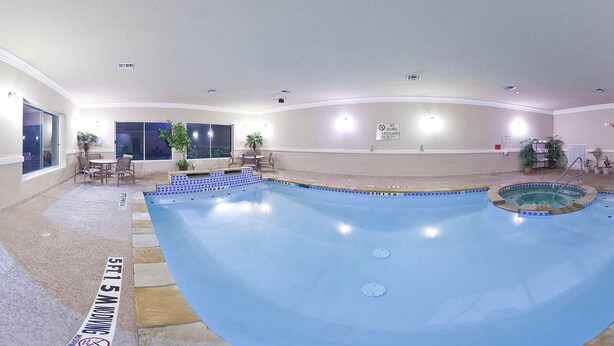 A large indoor swimming pool with a diving board, seating area, and a lifeguard on duty sign.