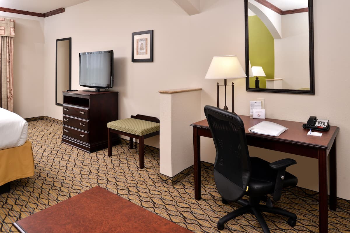 A hotel room with a bed, a desk with a chair, a television, a lamp, a telephone, and a small table with a chair.
