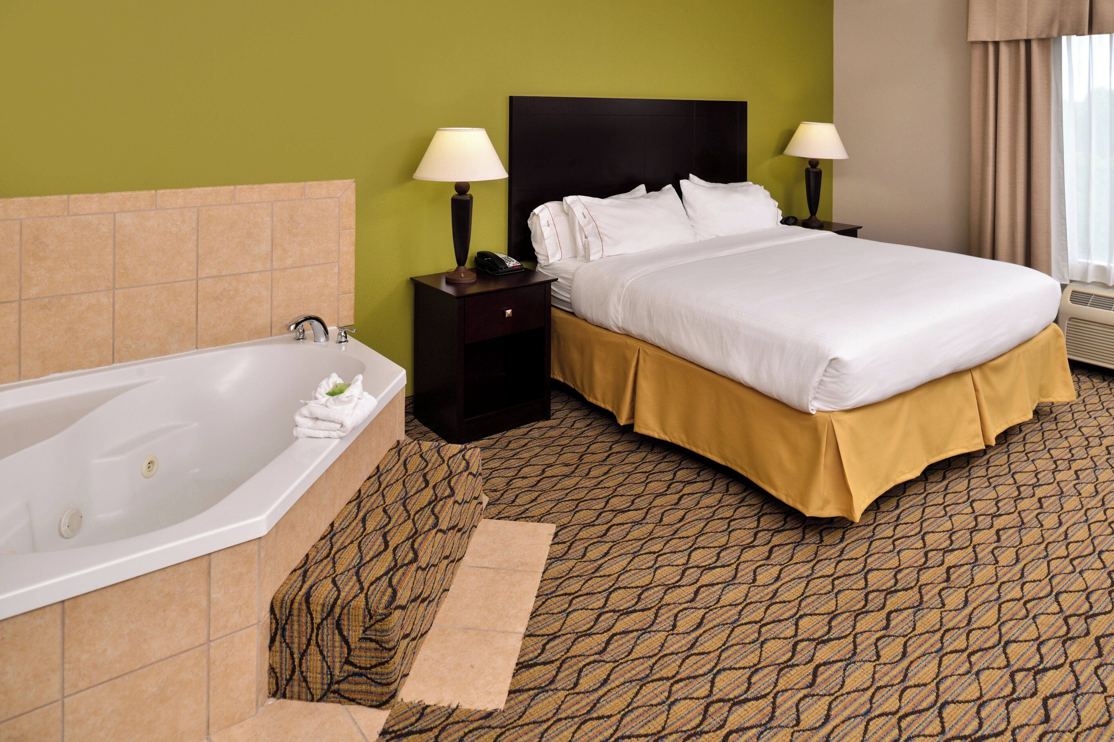 A hotel room with a large bed, a separate bathroom with a bathtub, and a patterned carpet.