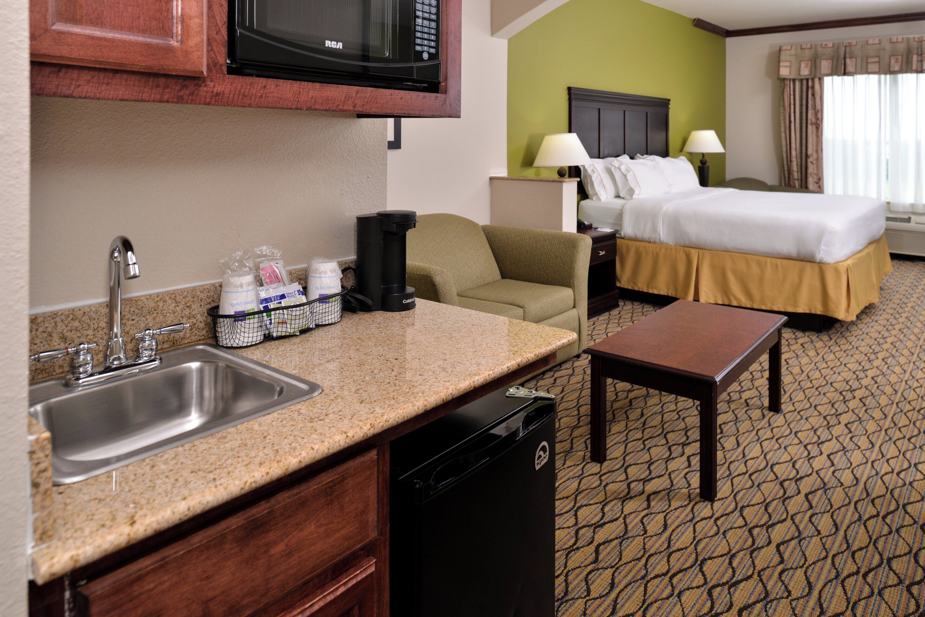 Una habitación de hotel con kitchenette, cama, escritorio y baño.