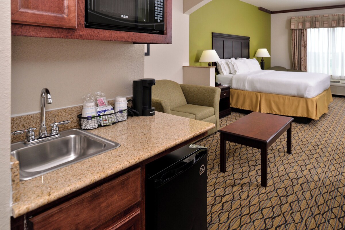 A hotel room with a kitchenette, a bed, a desk, and a bathroom.