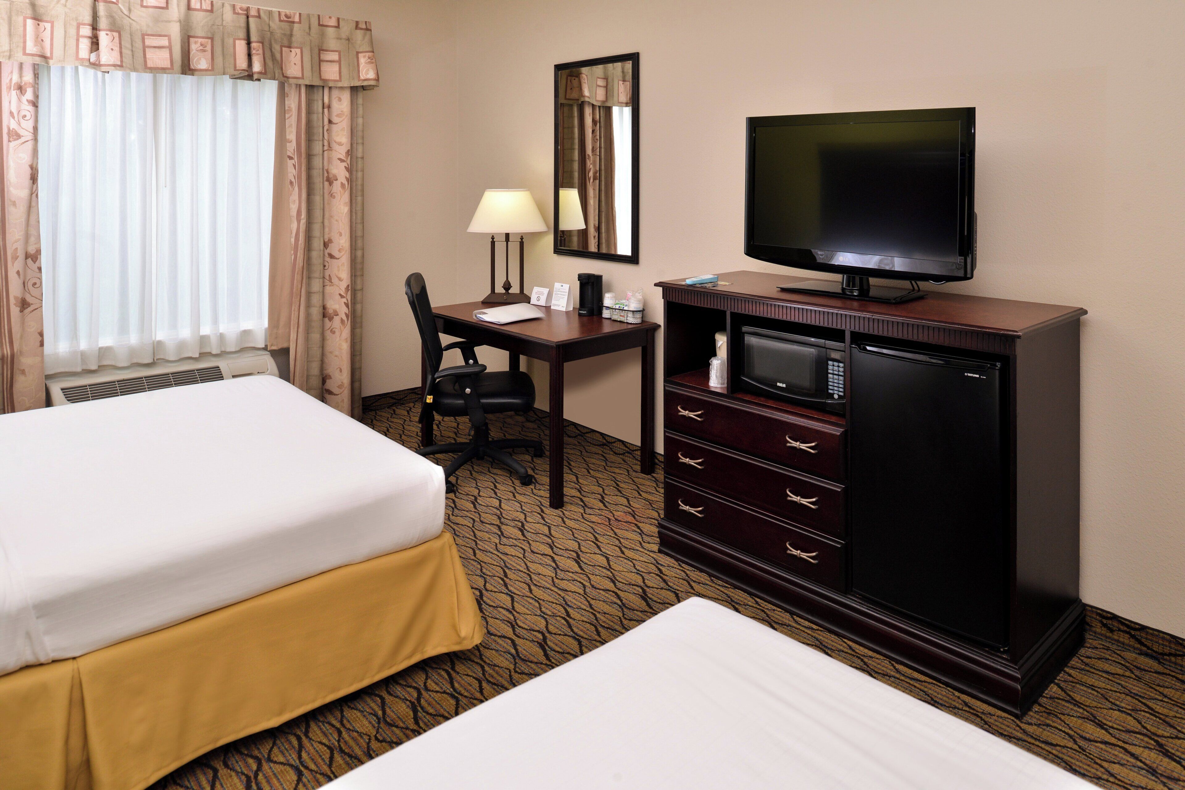 A hotel room with two beds, a desk with a computer, a television, and a minibar.