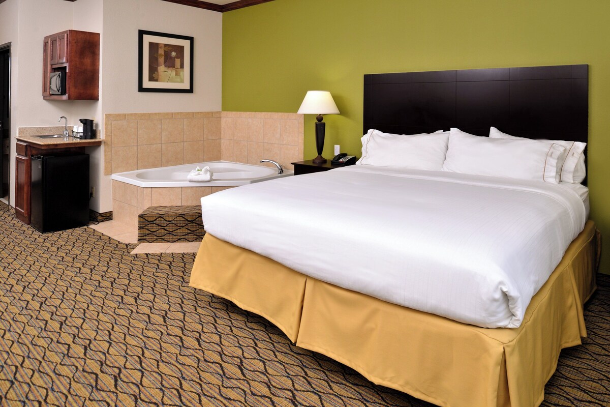 A hotel room with a large bed, a bathroom with a bathtub, a sink, and a small cabinet.
