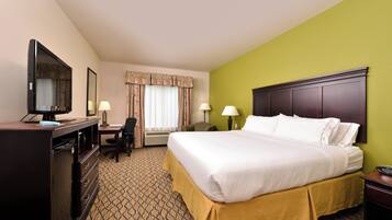 A hotel room with a bed, desk, TV, and a window with curtains.