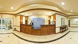 A reception area with a wooden reception desk, a glass door entrance, and a wall-mounted sign for the hotel.