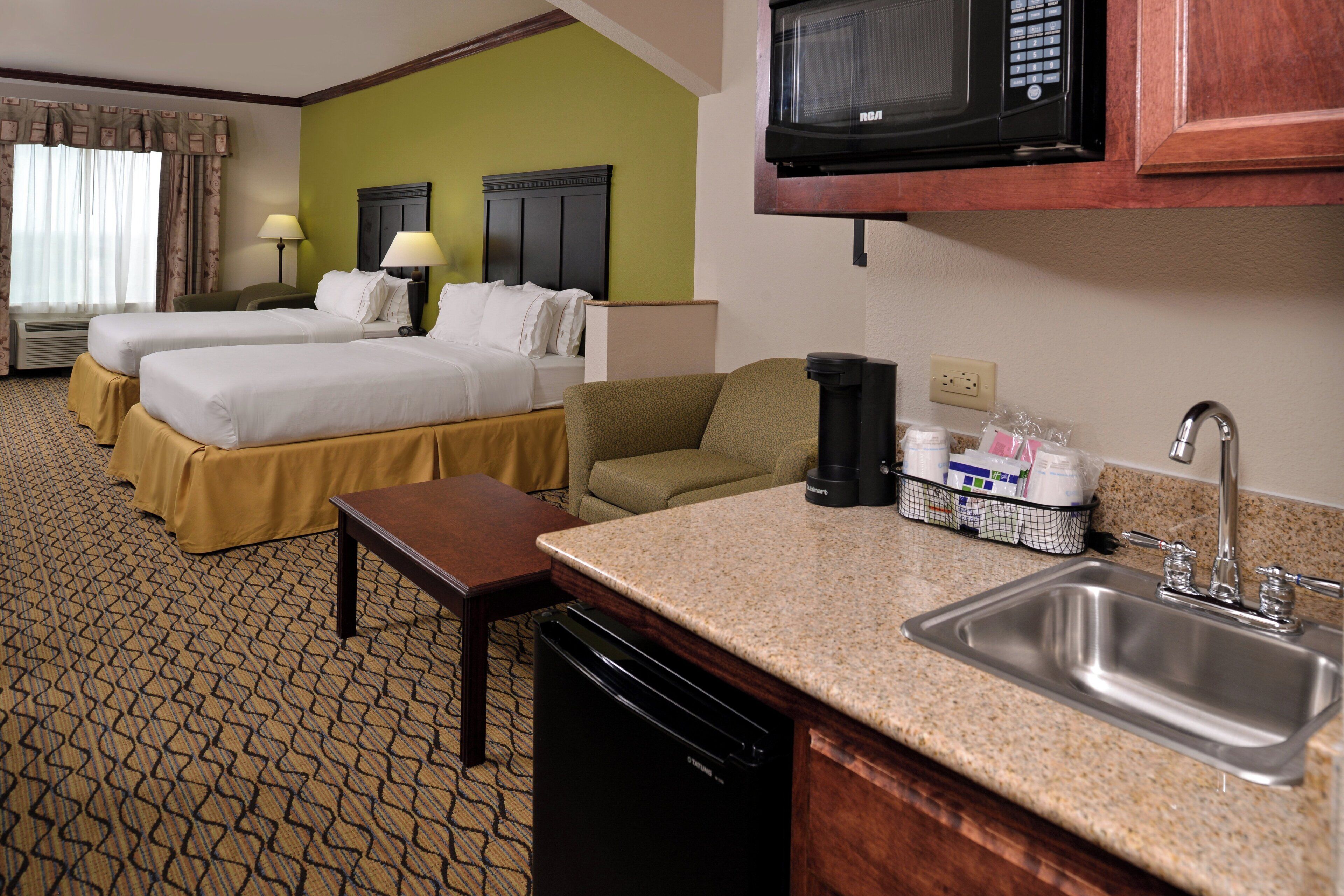 A hotel room with two beds, a kitchenette, a dining table, and a sofa.