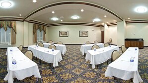 A conference room with white tables, chairs, and a patterned carpet.