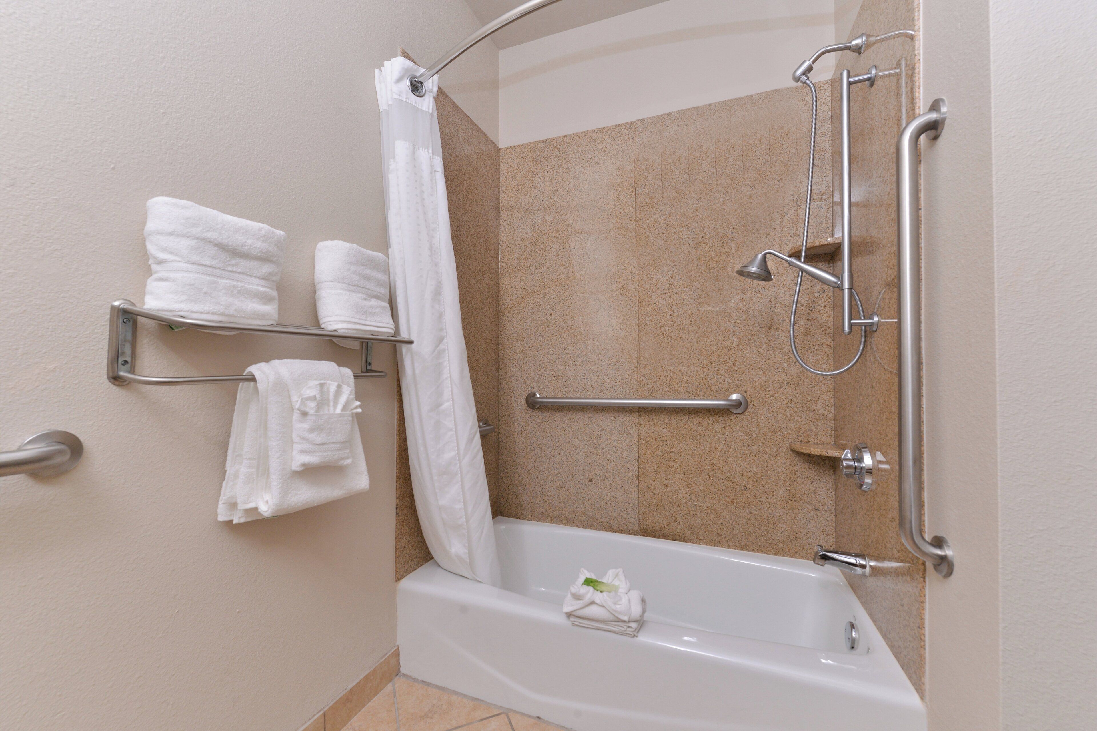 Un espace douche équipé d’une barre d’appui, d’un porte-serviettes avec des serviettes et d’un rideau de douche.