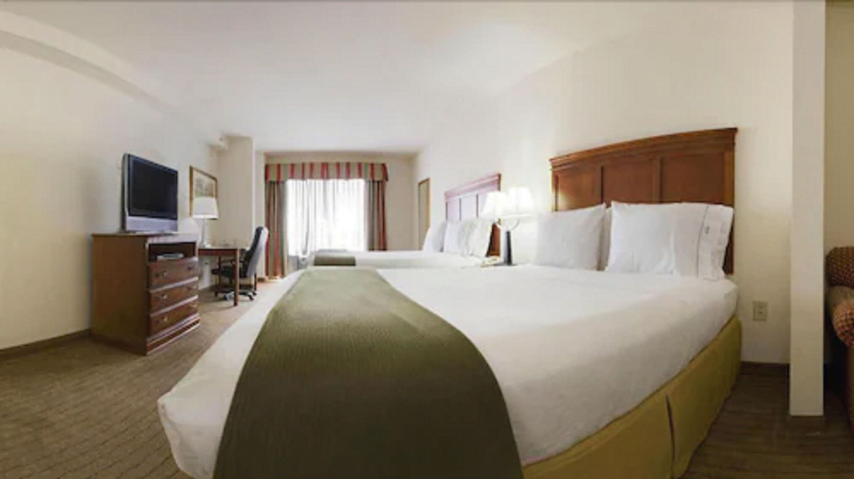 Une chambre d’hôtel avec un grand lit, un bureau avec une chaise, une télévision et une armoire.