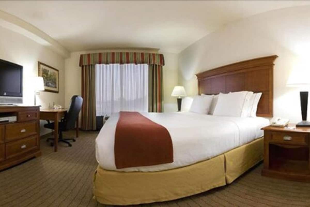 Una habitación de hotel con una cama grande, un escritorio con silla, un televisor y una ventana con cortinas.