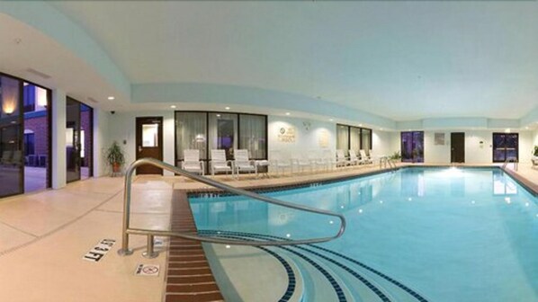 Piscina interior com linha d'água transparente, escada de acesso e espreguiçadeiras ao longo da borda.
