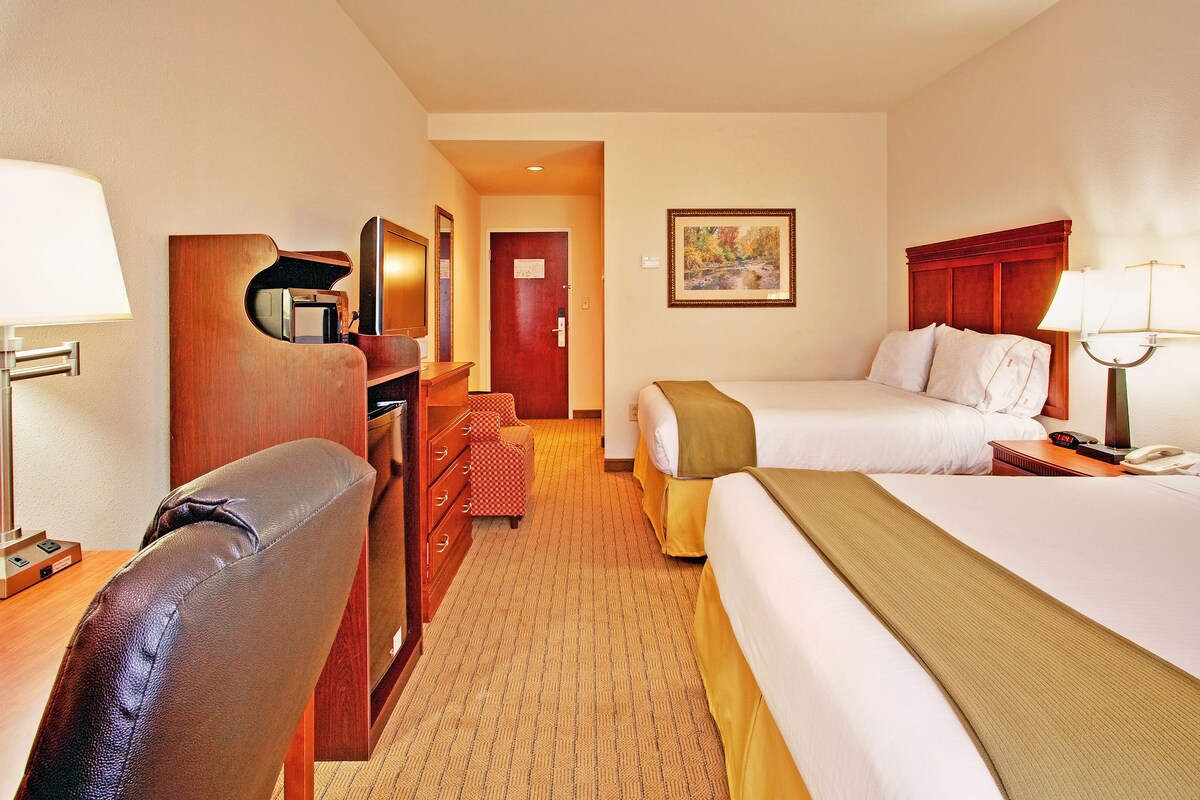 A hotel room with two beds, a desk with a lamp, a chair, and a painting on the wall.
