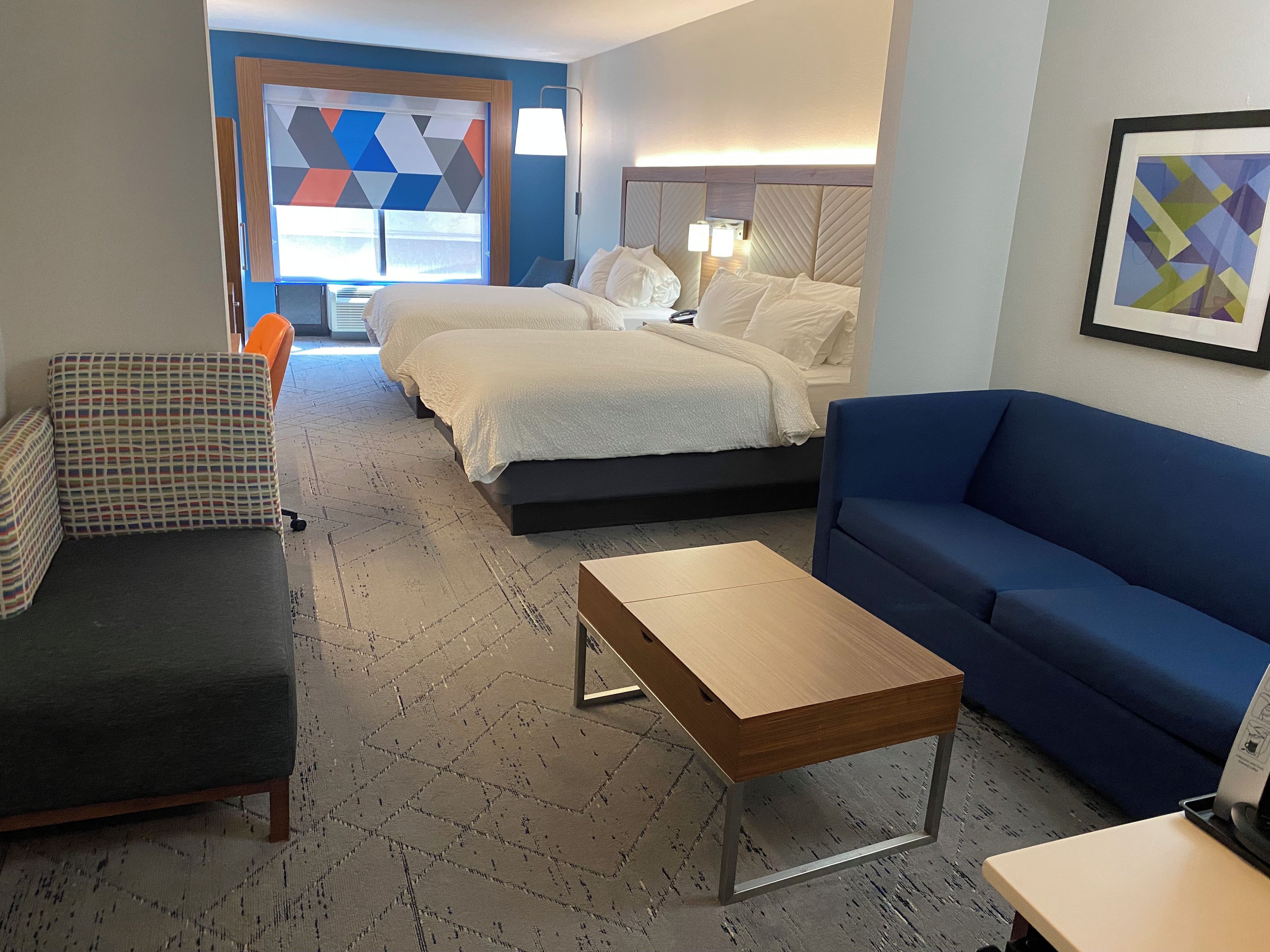 Una habitación de hotel con una cama, un sofá azul, una mesita y un sillón estampado.