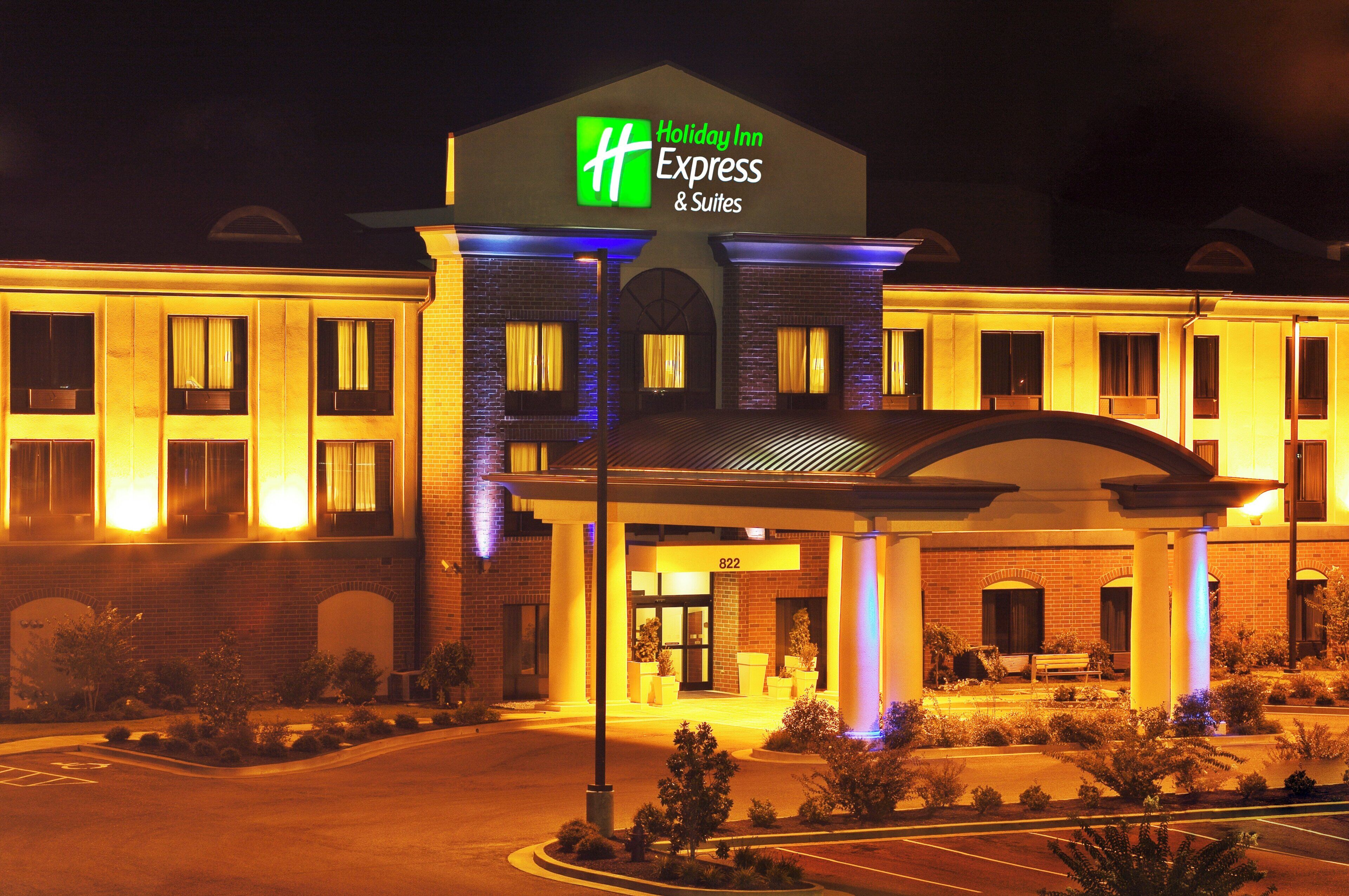 A Holiday Inn Express & Suites hotel with a brick facade, illuminated signage, and a covered entrance.