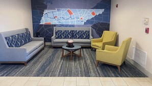 A lobby with a grey sofa, a yellow armchair, a round coffee table, and a wall map. - Holiday Inn Express Hotel & Suites Dyersburg by IHG (Dyersburg)