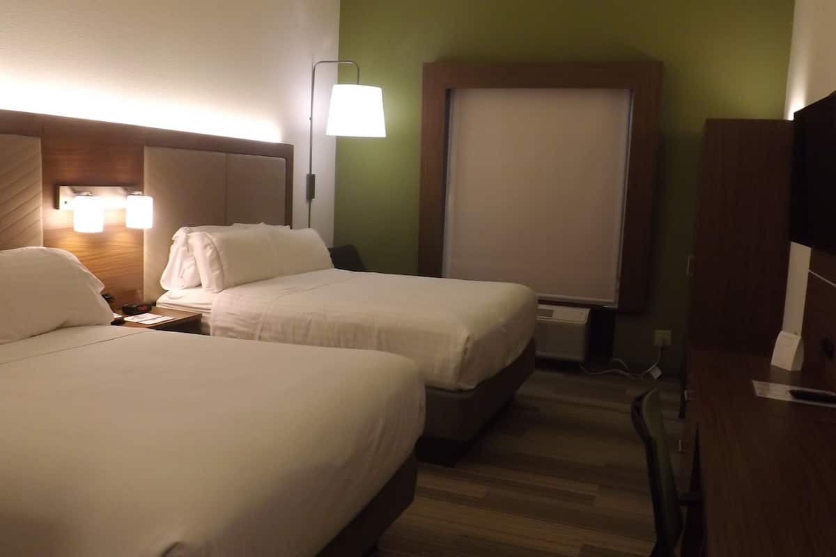Habitación de hotel con dos camas, un escritorio, una silla, un televisor y una ventana con vistas.
