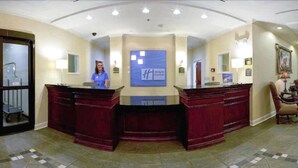A reception desk with a blue sign, a person standing behind it, and a framed picture on the wall. - Holiday Inn Express Hotel & Suites Dyersburg by IHG (Dyersburg)