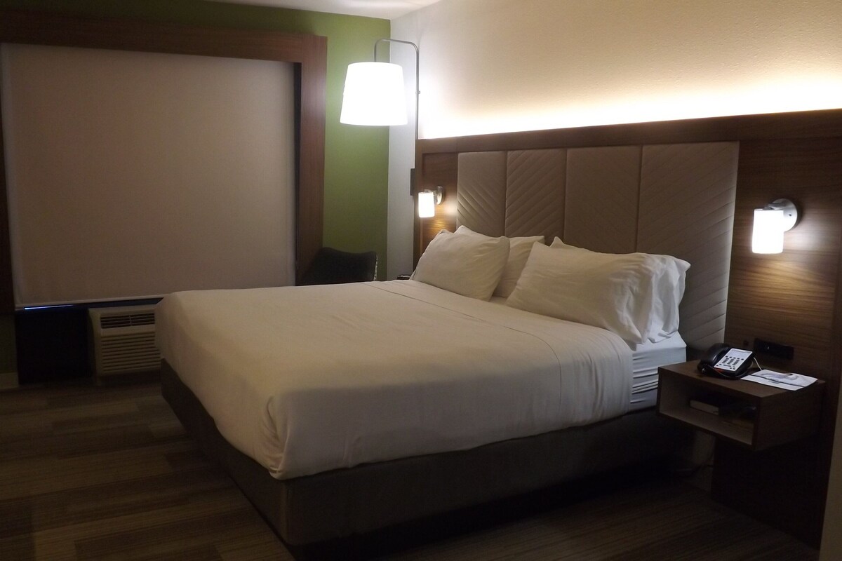 A hotel room with a bed, bedside table, lamp, and a wall-mounted phone.