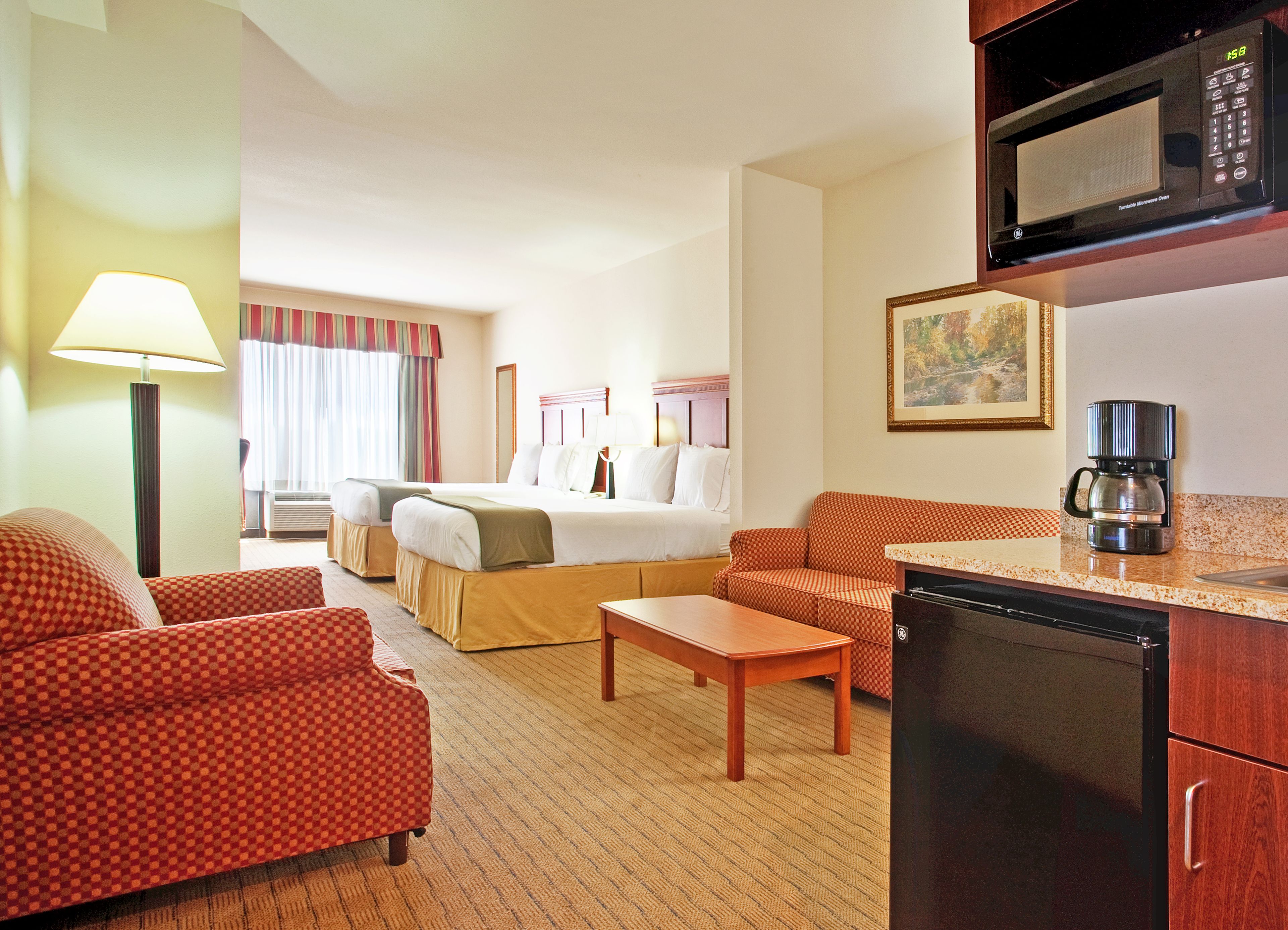 A hotel room with a bed, two armchairs, a coffee maker, a microwave, and a refrigerator.