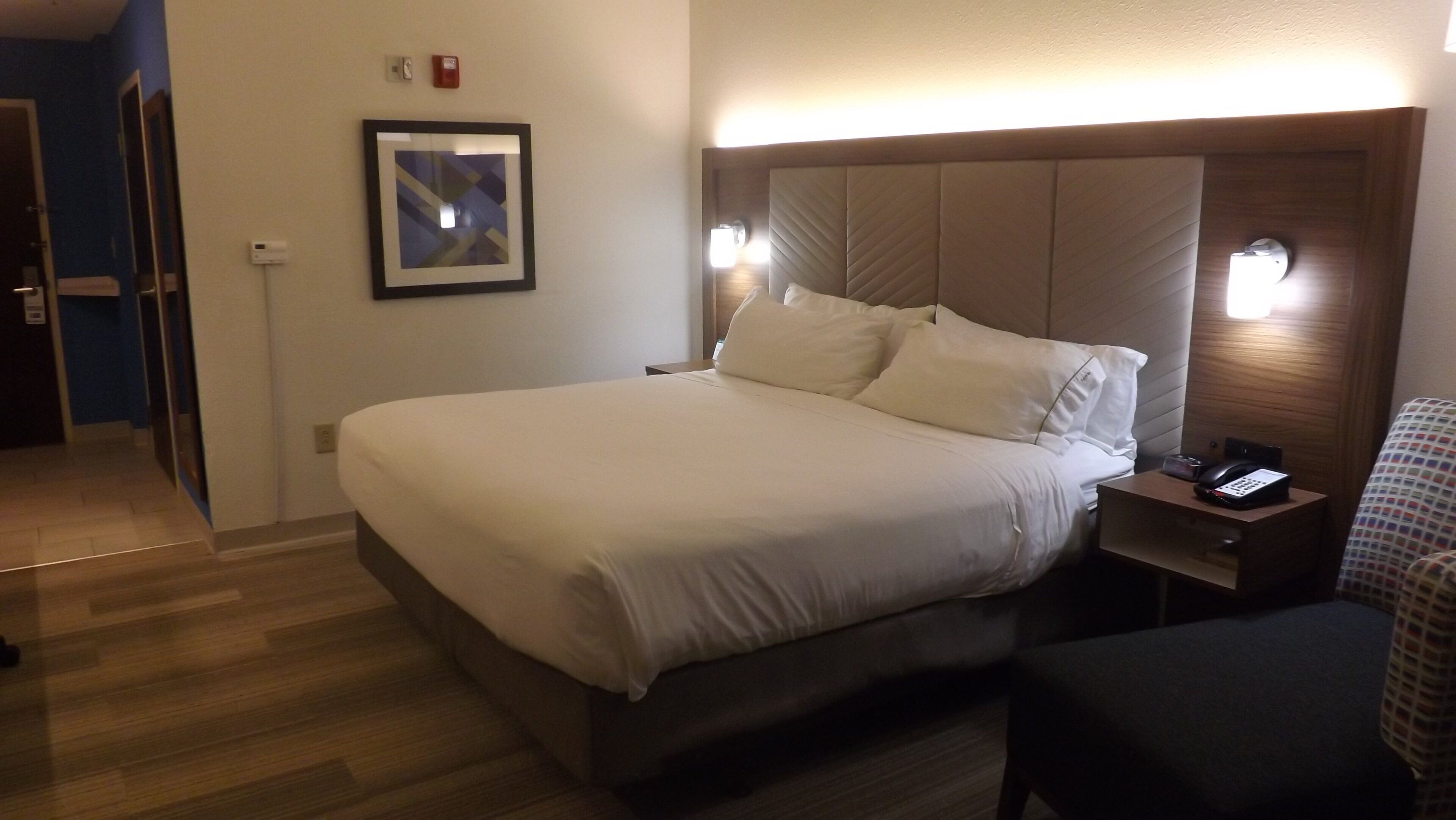 Hotellihuone, jossa on suuri sänky, yöpöytälamput, puhelin ja seinällä oleva taulu.