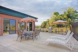 Un espacio al aire libre con patio, un edificio de ladrillo, una mesa con sillas y una parrilla.