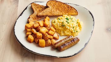 Um prato com torradas, ovos mexidos, batata palha e salsichas.