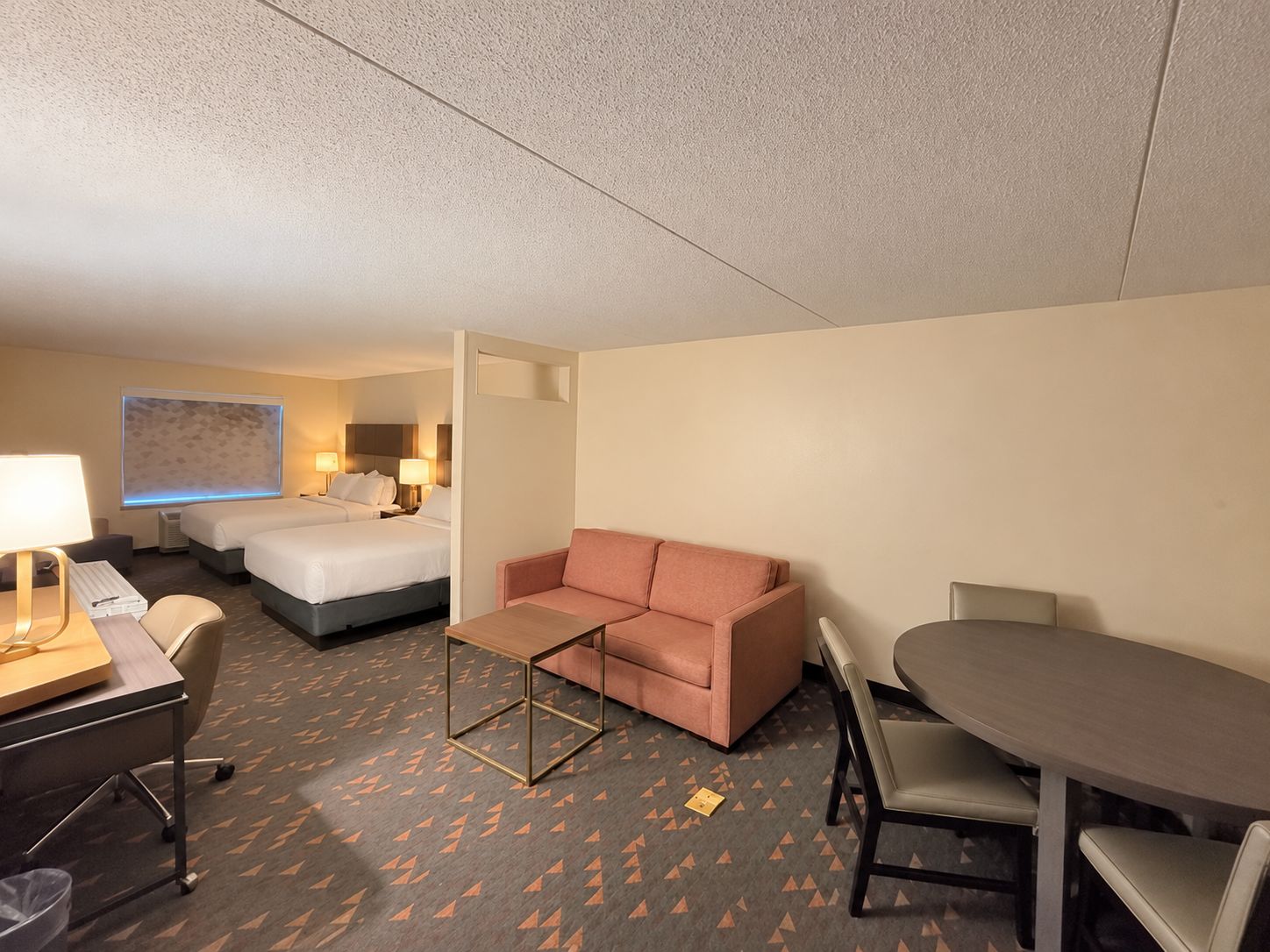 Habitación de hotel con una cama, un sofá, un escritorio con silla y una mesa de comedor con sillas.