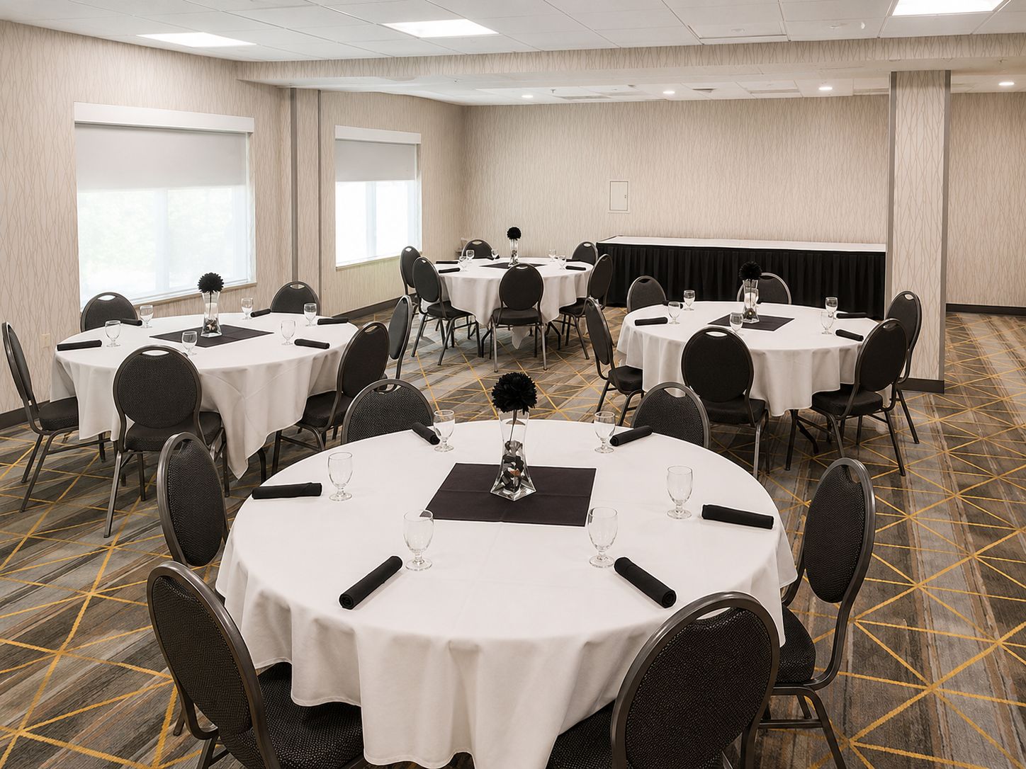 A conference room with multiple round tables, each with chairs, white tablecloths, and glassware.