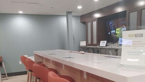 Zona de bar con una barra alargada, taburetes rojos y un cartel que indica los horarios del desayuno y la cena.