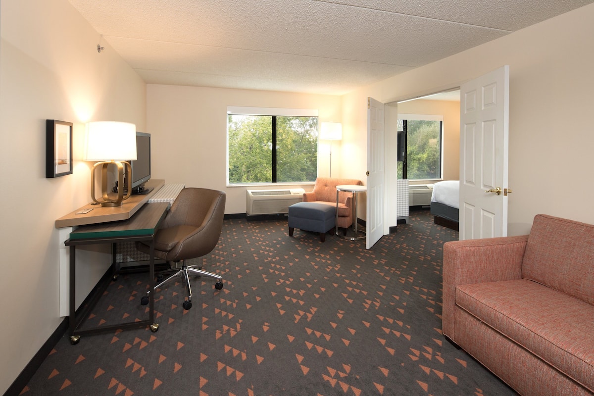 A hotel room with a desk, chair, sofa, and a window with a view.