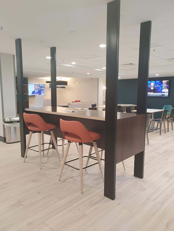 Ein moderner Konferenzraum mit einem langen Tisch, zwei roten Stühlen und einem Fernseher, der Nachrichten zeigt.