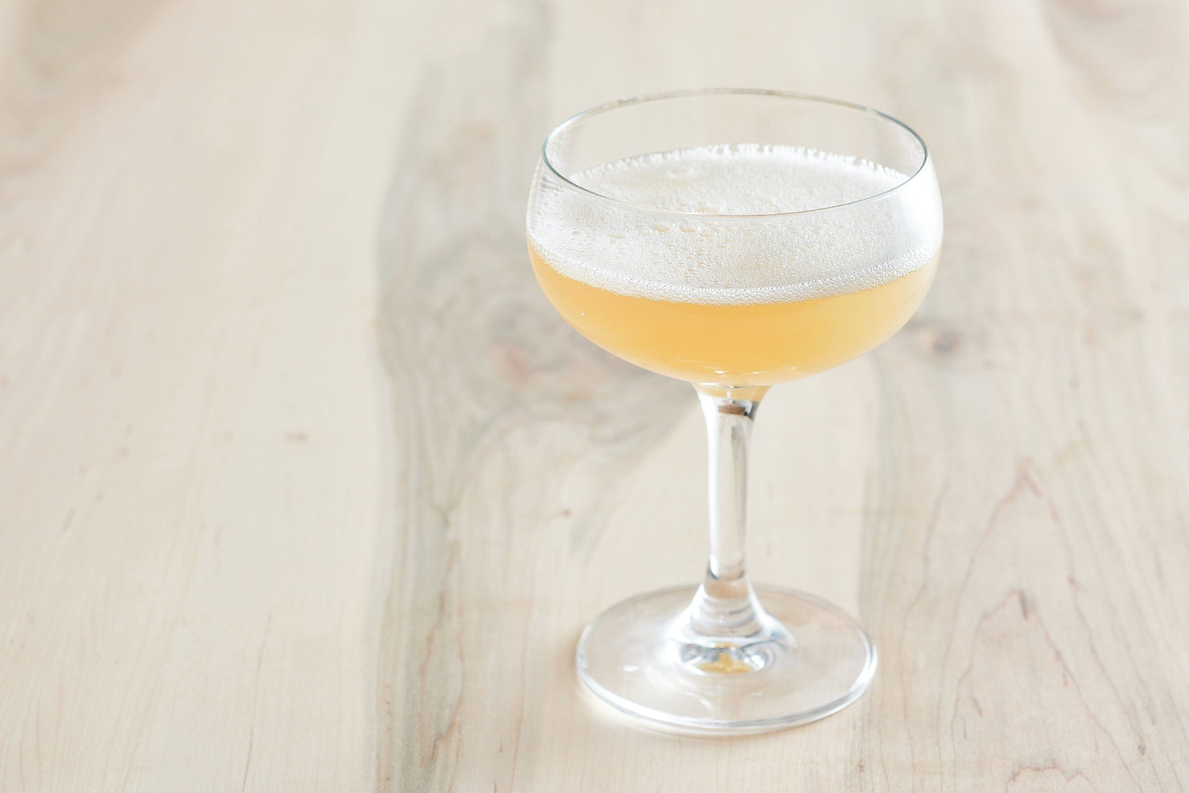 A clear glass with a golden liquid, likely a cocktail, on a wooden surface.