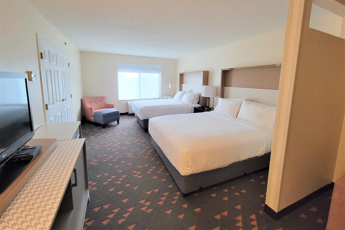 A hotel room with two beds, a TV, a desk, and a chair.