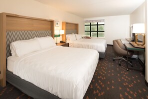 A hotel room with two beds, a desk, a chair, a lamp, and a window with a view of trees. - Holiday Inn & Suites Ann Arbor Univ Michigan Area by IHG (Ann Arbor)