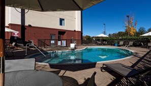 A swimming pool with lounge chairs and umbrellas, surrounded by a brick patio and a building with a red facade. - Hampton Inn Statesville (Statesville)