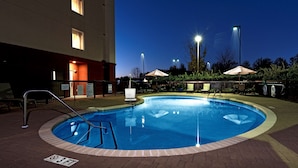 A swimming pool with a 3ft depth limit sign, surrounded by a brick patio, and adjacent to a building with illuminated windows.
